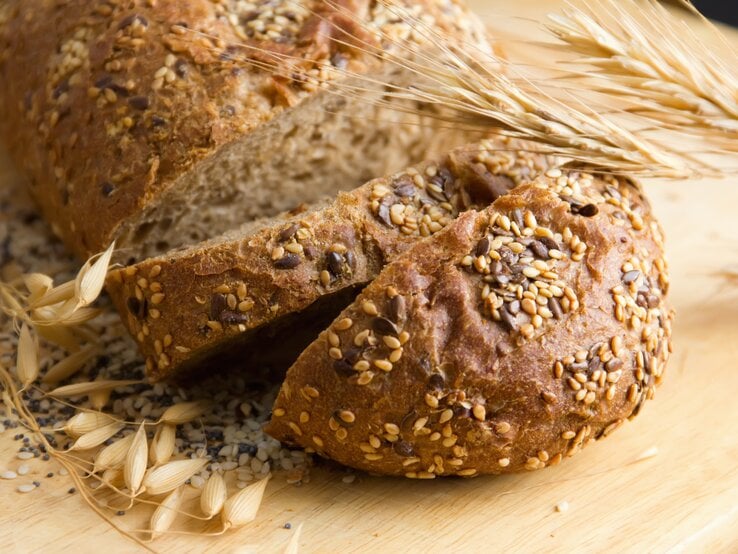 Das Proteinbrot auf einem hellen Schneidebrett nahe und mit frischem Getreide als Dekoration fotografiert.