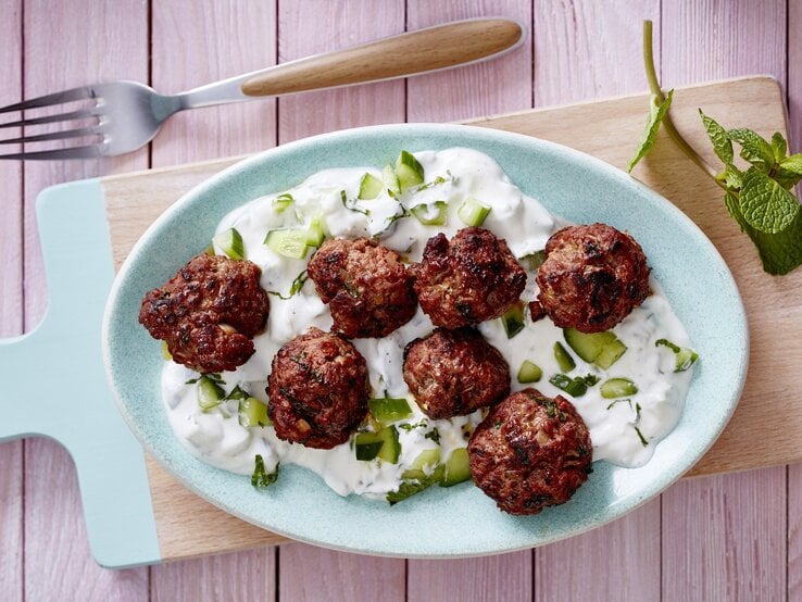 Hackbällchen mit Pfefferminze und Quark auf einem hölzernem Brett auf rosa Hintergrund.