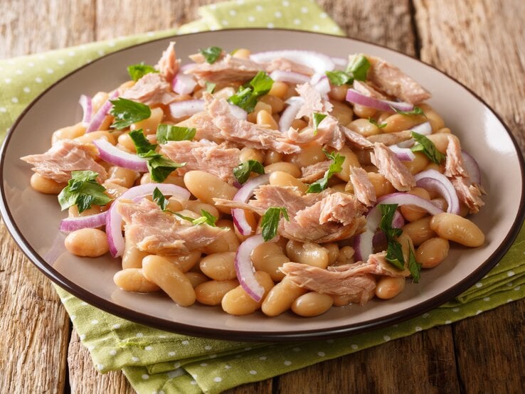 Bohnensalat mit Thunfisch und Zwiebeln auf einem Teller, angerichtet auf hölzernem Untergrund.