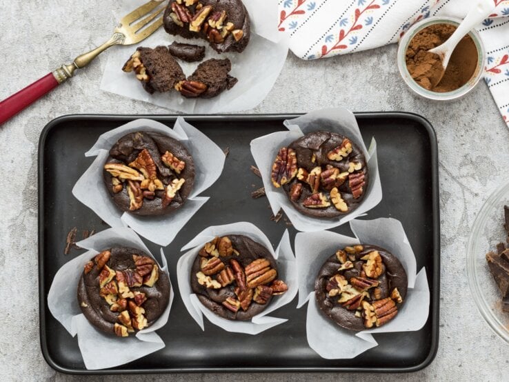 Die Schokomuffins mit Avocado und Nüssen auf einem Blech und grauem Tisch. Alles direkt von oben fotografiert.