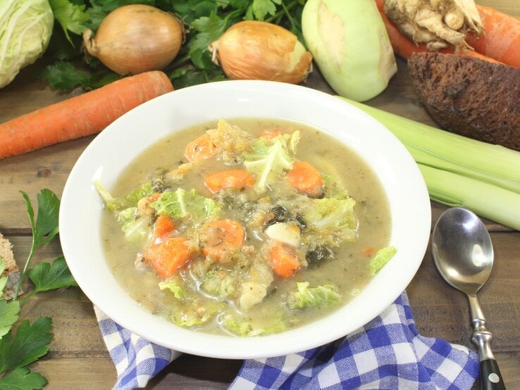 Wirsing-Kartoffel-Eintopf in einem Teller / Drumherum frisches Suppengemüse / Draufsicht, schräg