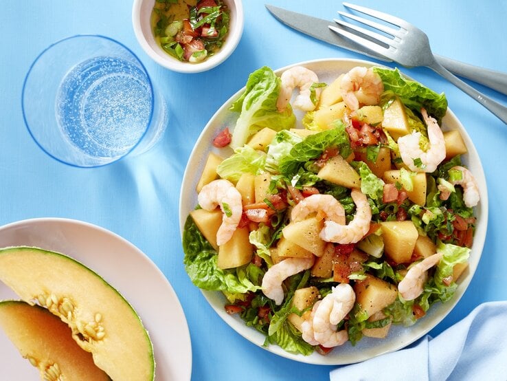 Melonensalat mit Garnelen auf weißen Tellern auf blauem Hintergrund.
