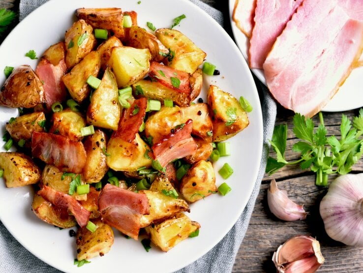 Ein Teller mit gebratenem Kohlrabi, Speckstreifen und frischen Frühlingszwiebeln, umgeben von frischen Kräutern.