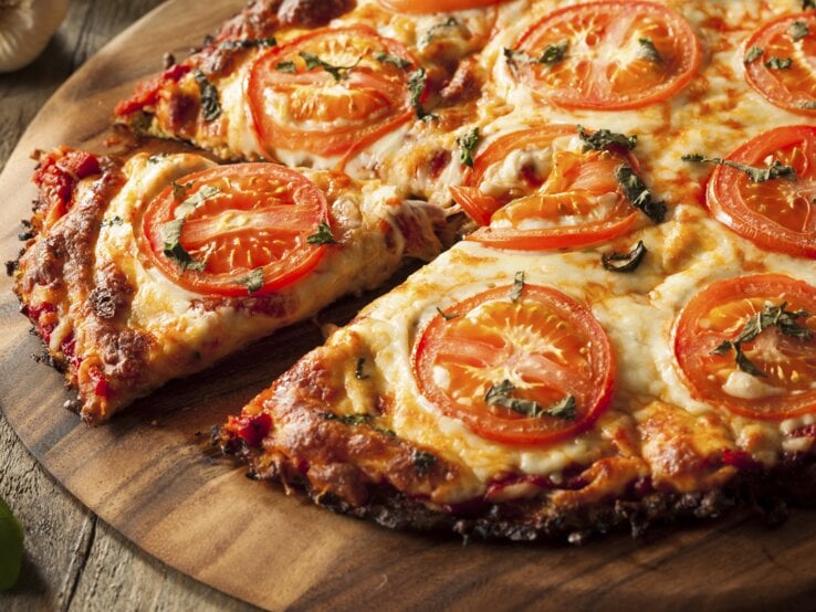 Nahaufnahme der Blumenkohl-Pizza auf einem rustikalen Holztisch mit Tomaten und Basilikum.