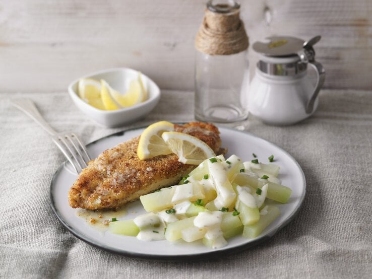 Ein weißer Teller mit dem Mandel-Schnitzel und Kohlrabi-Rahm auf einem hellen Tisch mit Zitronenecken garniert. | © StockFood / Gräfe & Unzer Verlag / Kramp + Gölling