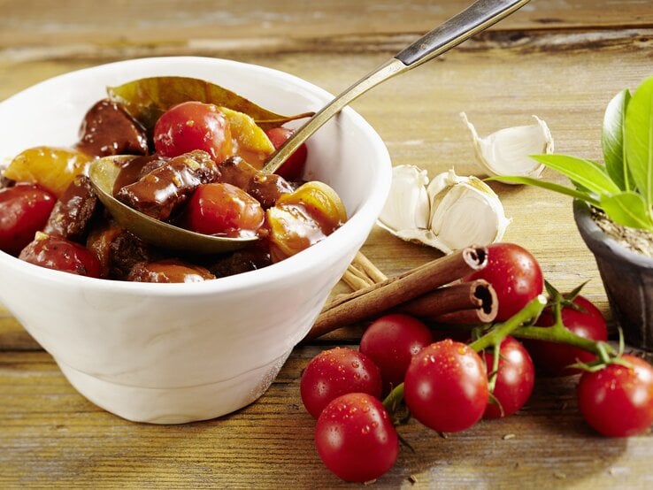 Ein weißes Schälchen mit dem griechischen Eintopf auf einem Holztisch fotografiert.