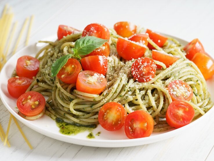 Pesto-Spaghetti-Salat mit Tomaten auf weißem Teller.