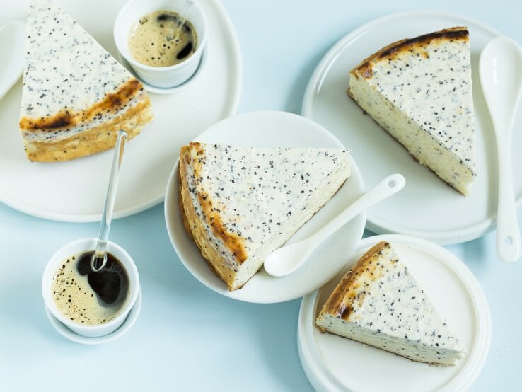 Mehrere Stücken vom Käsekuchen auf weißem Geschirr und einer hellblauen Tischdecke. Daneben noch Kaffee in kleinen Tassen. Alles direkt von oben fotografiert. | © StockFood / Gräfe & Unzer Verlag / D'Angelo, Vivi