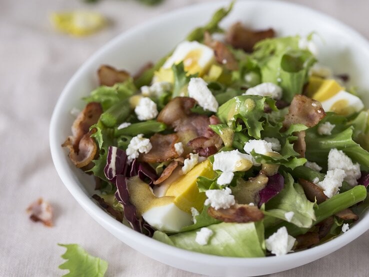 Spargelsalat mit Ei, Speck und Feta auf einem Teller.
