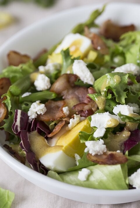 Spargelsalat mit Ei, Speck und Feta auf einem Teller.