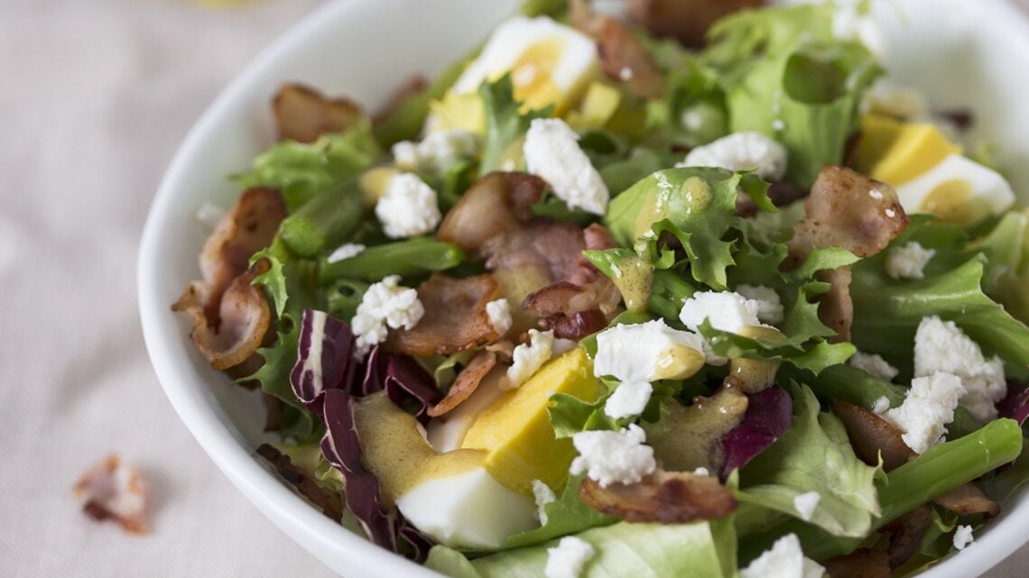 Spargelsalat mit Ei, Speck und Feta auf einem Teller.