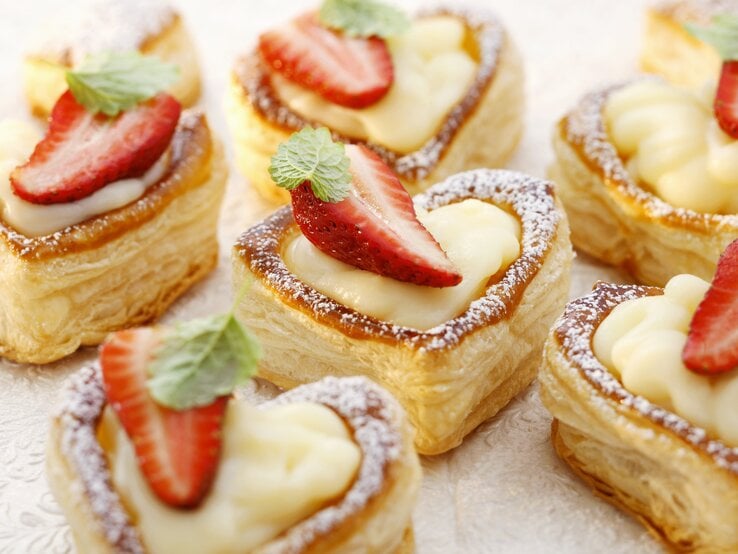 Draufsicht schräg: mehrere Vanillepudding im Blätterteigherz mit Erdbeeren.