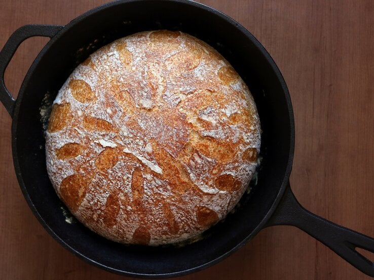 Knuspriges Topfbrot in einem Gusseisentopf. Der Topf steht auf einem braunen hölzernen Untergrund. 