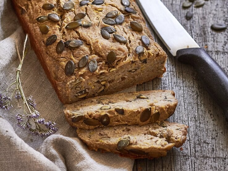 Ein angeschnittenes Zucchinibrot mit Banane. Daneben liegt ein großes Küchenmesser.