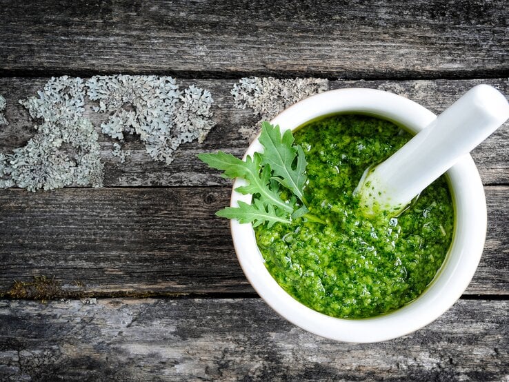 Weiße Schale gefüllt mit Rucola-Pesto auf grauer Holz-Oberfläche. 