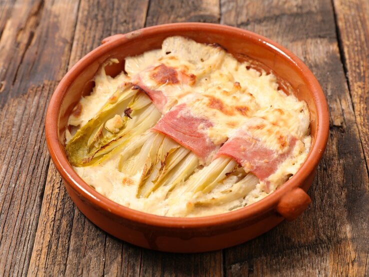 Ein braune Auflaufform mit dem Gericht auf einem dunklen Holztisch von schräg oben fotografiert. | © iStock/margouillatphotos