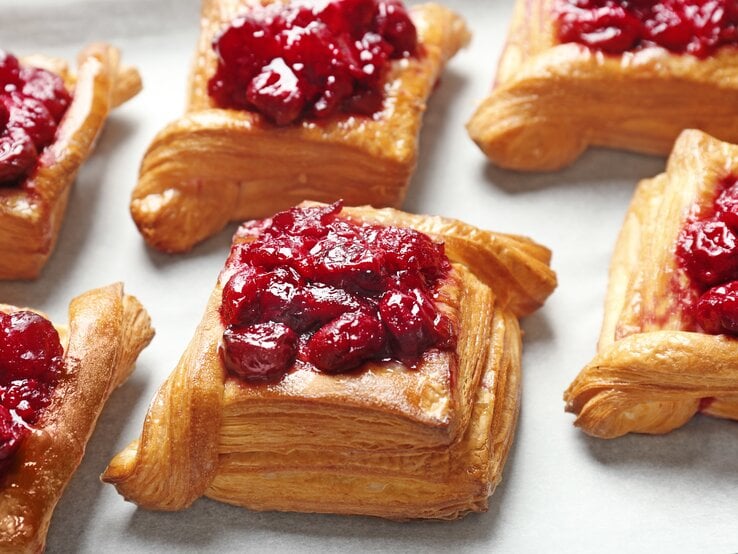 Frontal: Gefüllte Kirschtaschen aus Blätterteig liegen auf einem weißem Untergrund.