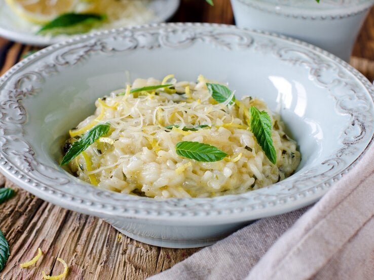 Ein tiefer Pasta-Teller mit Risotto mit Zitrone und Minze auf einem Holztisch.