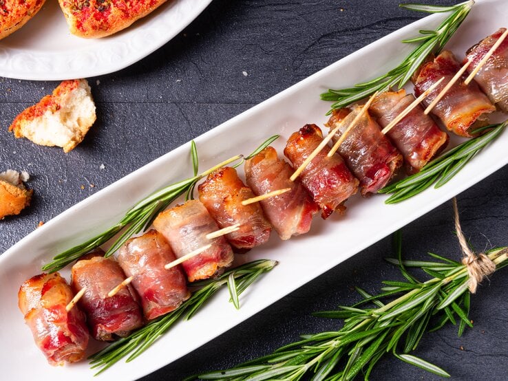 Weißer langer Teller mit gefüllten Datteln im Speckmantel, daneben Thymian-Zweige