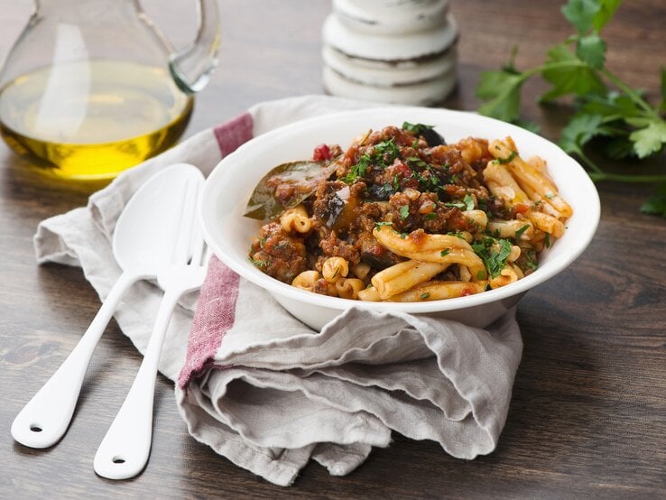 Ein weißer, tiefer Teller mit dem Pastagericht auf einem rustikalen Holztisch.