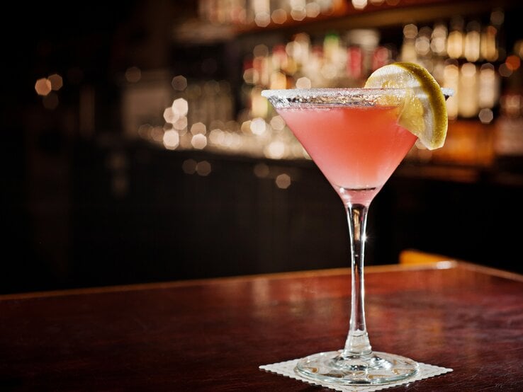 Ein liebevoll dekoriertes Glas mit Cosmoolitan in einer dunkleren Bar-Atmosphäre. | © iStock/VectaPhoto