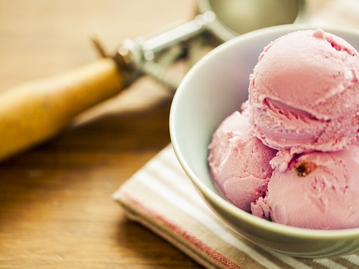 Mehrere Bällchen Erdbeer-Käsekuchen-Eis in einer weißen Schale. 