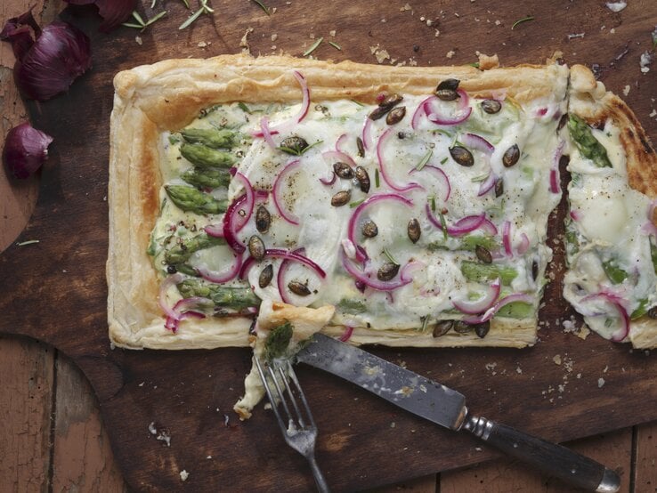 Ein dunkles Holzbrett mit der Tarte auf einem Holztisch direkt von oben fotografiert. | © Stockfood
