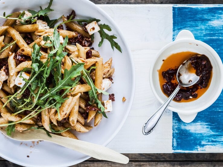 Ein weißer Teller mit dem Nudelsalat auf einem weiß-blauen Tisch direkt von oben fotografiert. | © StockFood