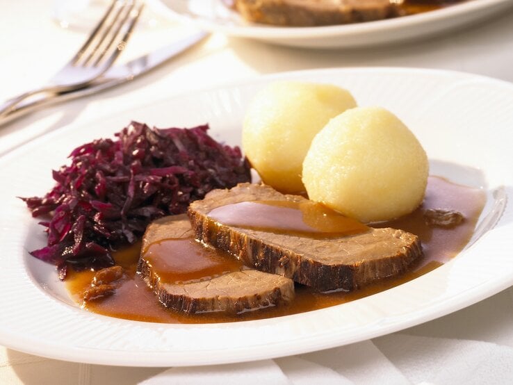 Rheinischer Sauerbraten mit Rotkohl und Kartoffelklößen auf weißem Teller.  | © StockFood / Rees, Peter