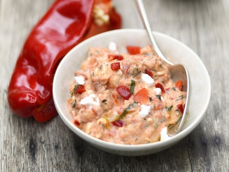Eine weiße Schale mit dem rötlichen Dip auf einem alten Holztisch. Alles von der Seite fotografiert.