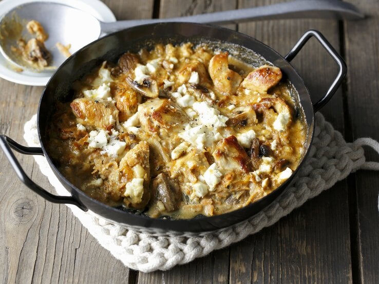 Eine gusseiserne Pfanne mit dem Gericht auf einer beigen Tischdecke und rustikalem Holztisch. Alles schräg oben von der Seite fotografiert. | © StockFood / Gräfe & Unzer Verlag / mona binner PHOTOGRAPHIE