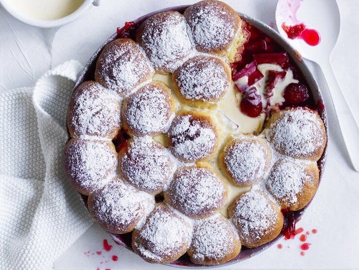 Draufsicht: Ein Rhabarber-Erdbeer-Dessert mit Milchbrötchen und Vanillesoße in einer runden Form aus Metall.