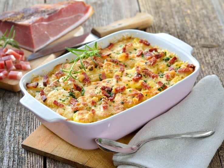 Eine weiße Auflaufform mit dem Gratin auf einem Holztisch von schräg oben fotografiert.