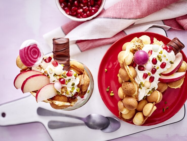 Eine große Bubble-Waffel auf einem runden Teller / eine kleine im Glas / zwei Teelöffel / Brettchen / Küchentuch / Draufsicht | © Eat Club; Isabell Triemer