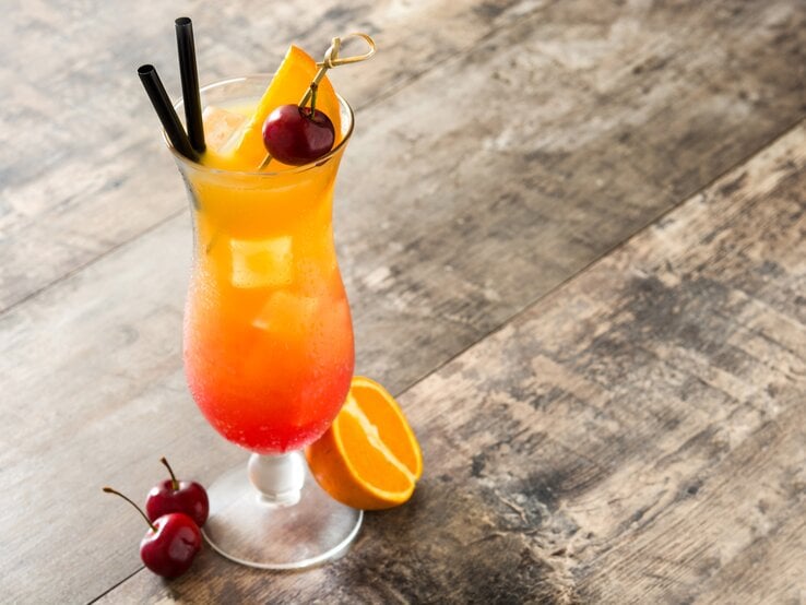 Liebevoll dekoriertes Glas gefüllt mit einem fruchtig aussehendem Cocktail auf Holztisch.  | © Shutterstock/etorres