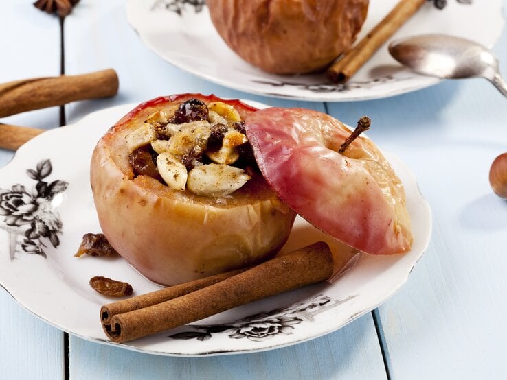 Ein gefüllter Bratapfel mit Knusperhaube auf weißem Teller. 