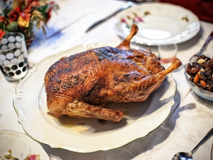 Gänsebraten mit Backpflaumen  auf einem Teller / Drumherum Teller, Besteck und weihnachtliche Dekoration | © iStock/gilotyna