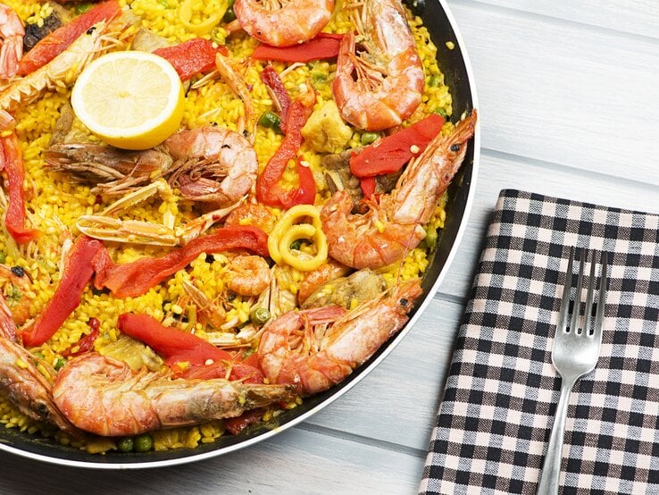 Eine schwarze Pfanne mit dem gelben Reis und Meeresfrüchten auf einem weißen Holztisch.