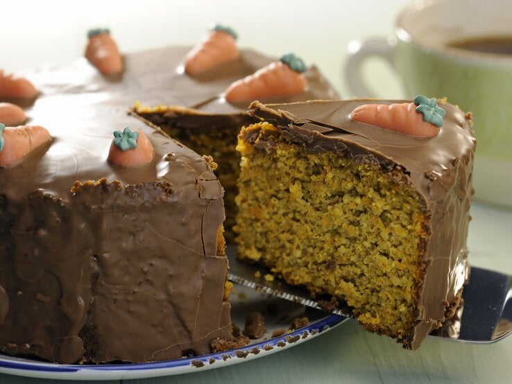 Eine Nahaufnahmen vom Schoko-Möhrenkuchen und gerade wird ein angeschnittenes Stück rausgenommen mit dem Tortenheber. | © iStock/Silberkorn