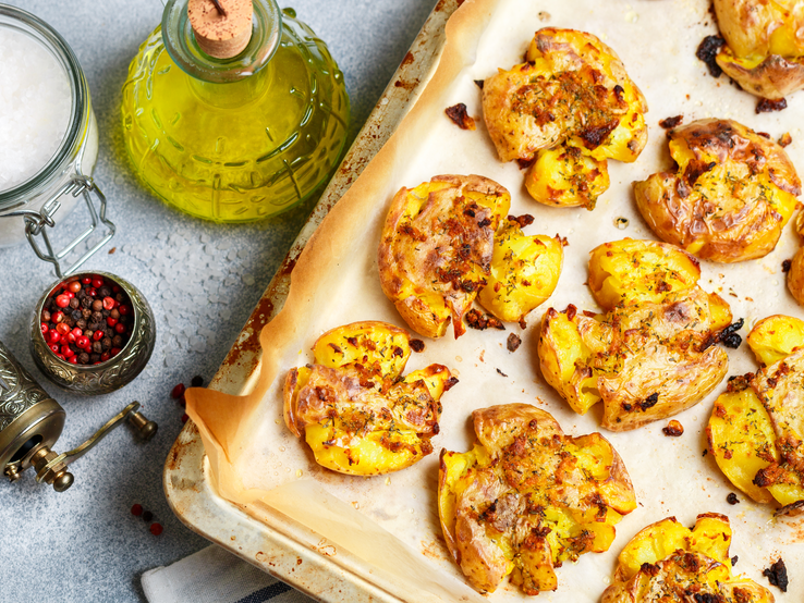 Smashed Potatoes mit Zutaten auf einem Backblech. | © Shutterstock/ Viktory Panchenko