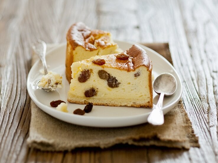 Weißer Teller, auf dem zwei Stücke Käsekuchen mit Rosinen liegen.  | © StockFood/Lanneretonne, Anthony