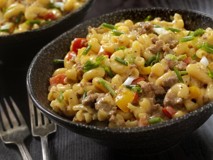 Dunkler, gemusterter Teller gefüllt mit cremigen Käsenudeln mit Hackfleisch. 