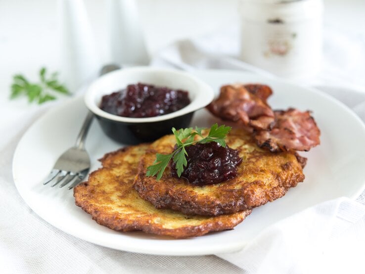 Zwei schwedische Kartoffelpfannkuchen mit Speck und Preiselbeeren auf hellem Teller. 