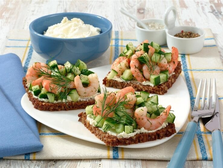 Drei Scheiben Vollkornbrot mit Frischkäse, Gurken und Garnelen.