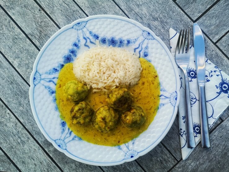 Draufsicht auf einen kitschigen Teller, darauf Hackbällchen in cremiger Soße und Reis.