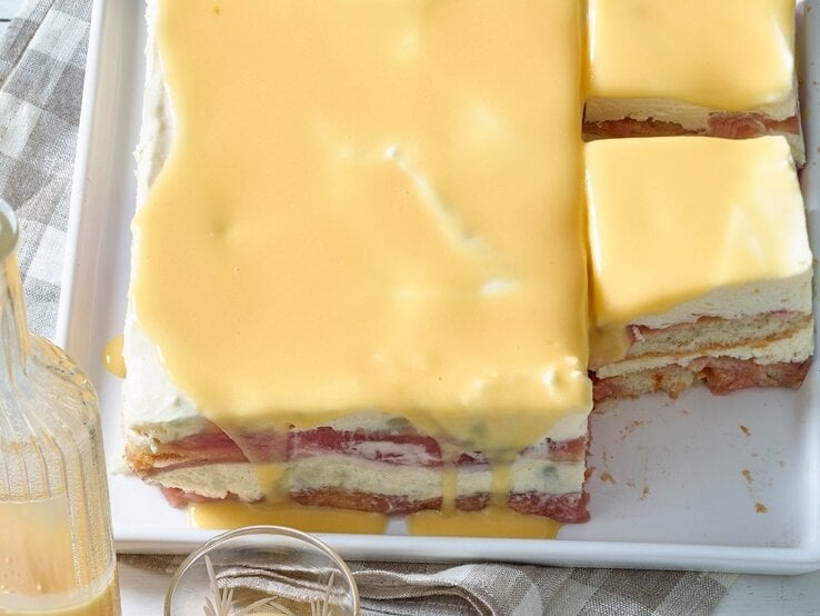 Draufsicht: Zwei angeschnittene gelbe Tiramisu mit Eierlikör auf einem Tisch. Davor steht eine Glasflasche, die mit einer hellen Flüssigkeit gefüllt ist.