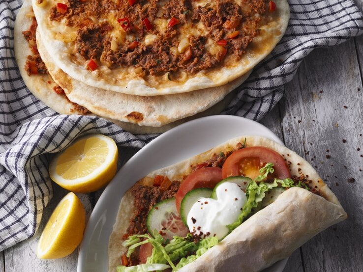 Draufsicht: Vier türkische Pizza Lahmacun. Drei nur mit Hackfleisch, eine mit Tomaten, Gurkenscheiben, Salat und Joghurtsauce