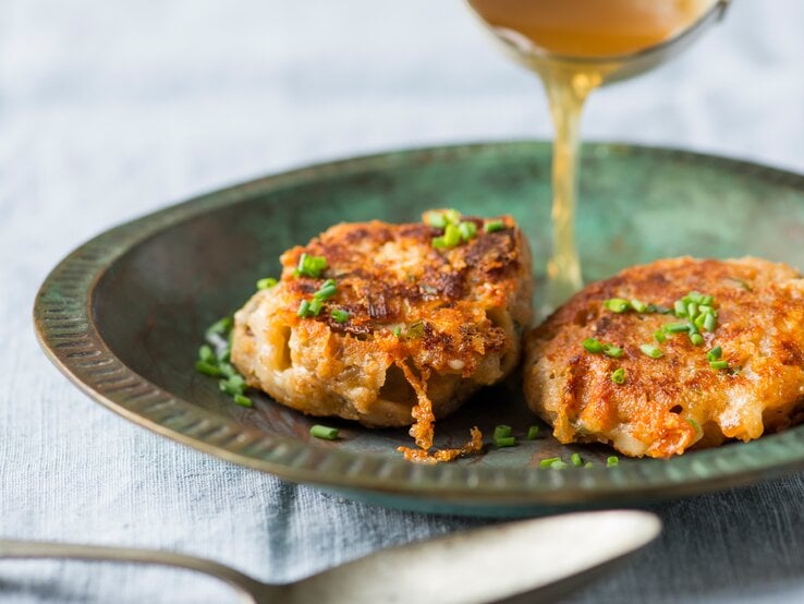 Zwei goldbraun gebratene Kaspressknödel liegen in einem dunkelgrünen, rustikalen Teller.