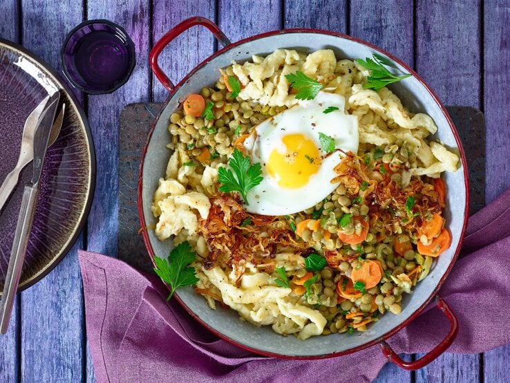 Spätzle-Linsenpfanne mit Spiegeleiern in einer Pfanne auf hölzernem Hintergrund. 