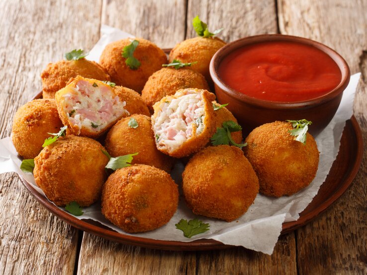 Runder Teller, darauf mehrere frittierte Schinken-Bällchen mit Sauerkraut, daneben ein tomatiger Dip. 